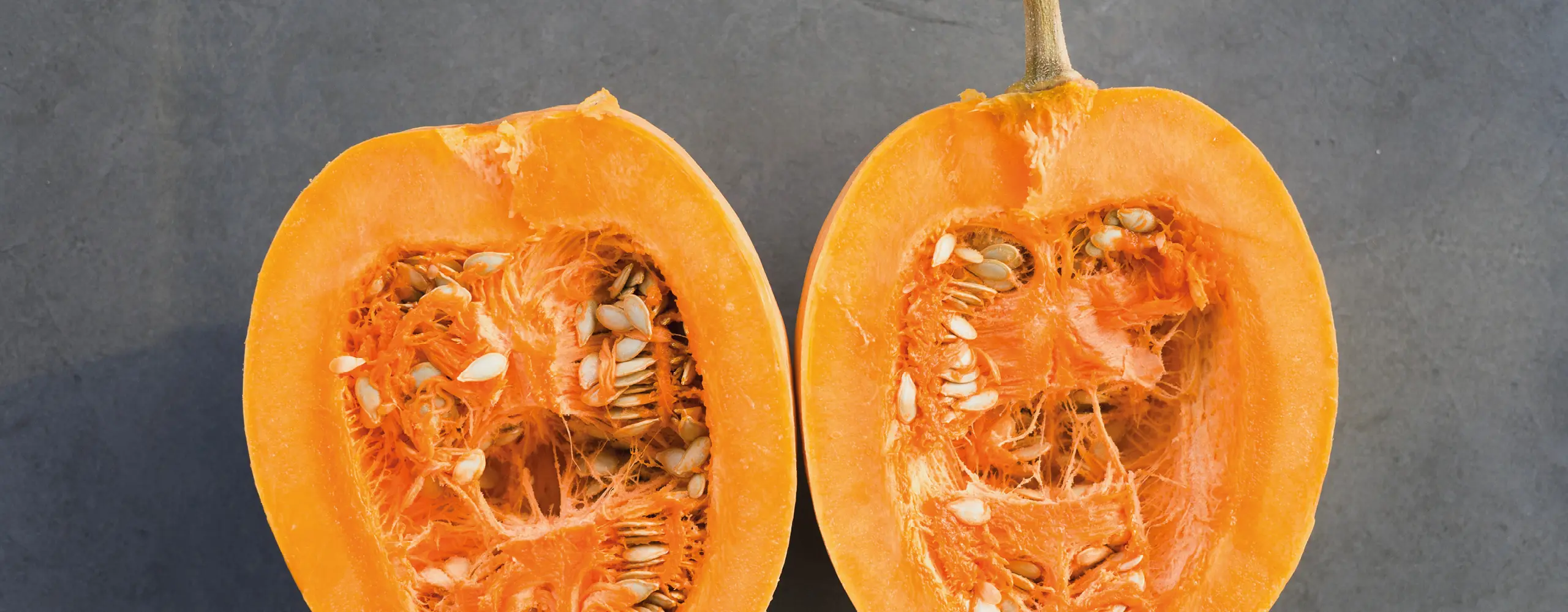 Aufgeschnittener Kürbis mit leuchtend orangefarbenem Fruchtfleisch und sichtbaren Kernen auf hellem Untergrund. Symbol für frisches Herbstgemüse, gesunde Ernährung und saisonales Kochen in der Küche.